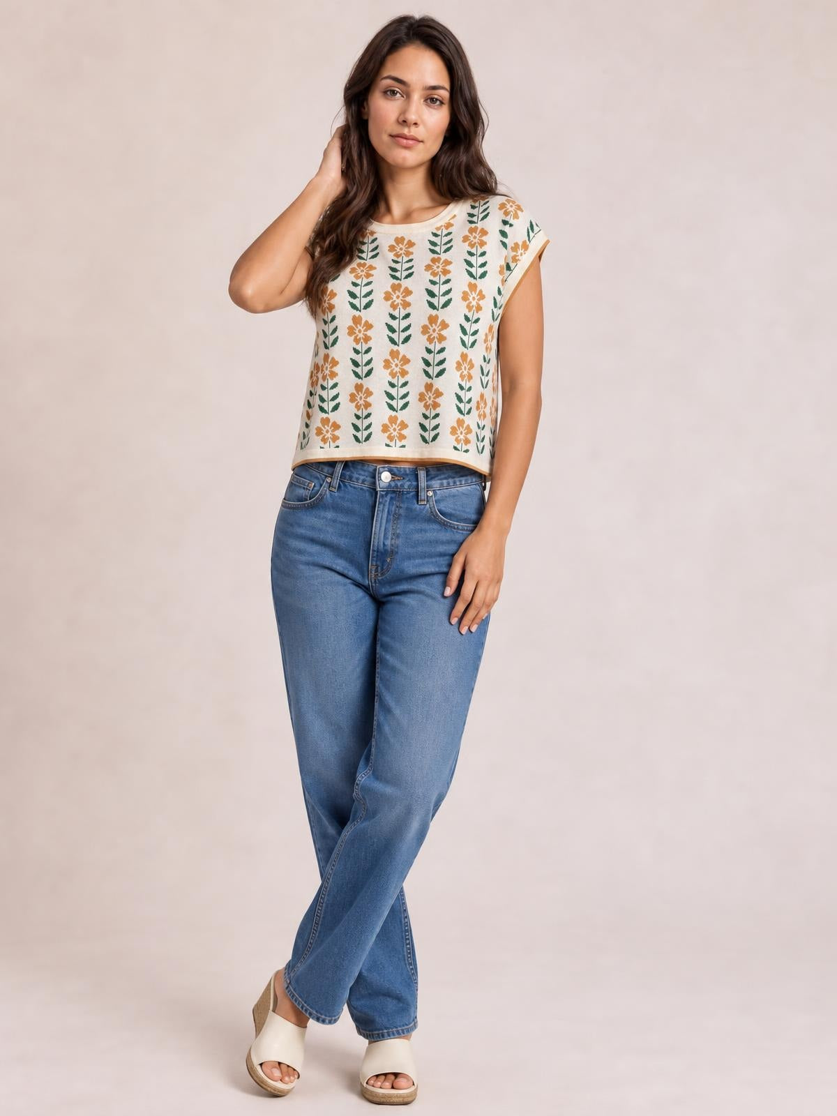 Model wearing a cream flower-print knit top with a round neck, short sleeves, and relaxed cropped silhouette, posing with one hand in her hair.