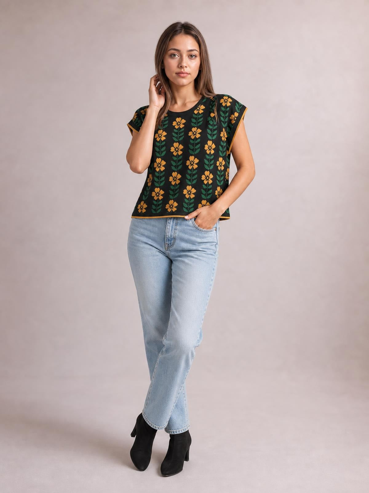 Model wearing a black flower-print knit top with a round neck, short sleeves, contrast trim, and a relaxed straight silhouette, posing with one hand in her pocket.