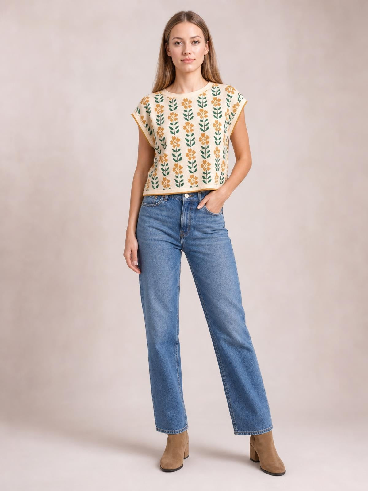Model wears a cream flower-print knit top with a round neck, short sleeves, and relaxed boxy silhouette, standing with one hand in her jeans pocket.