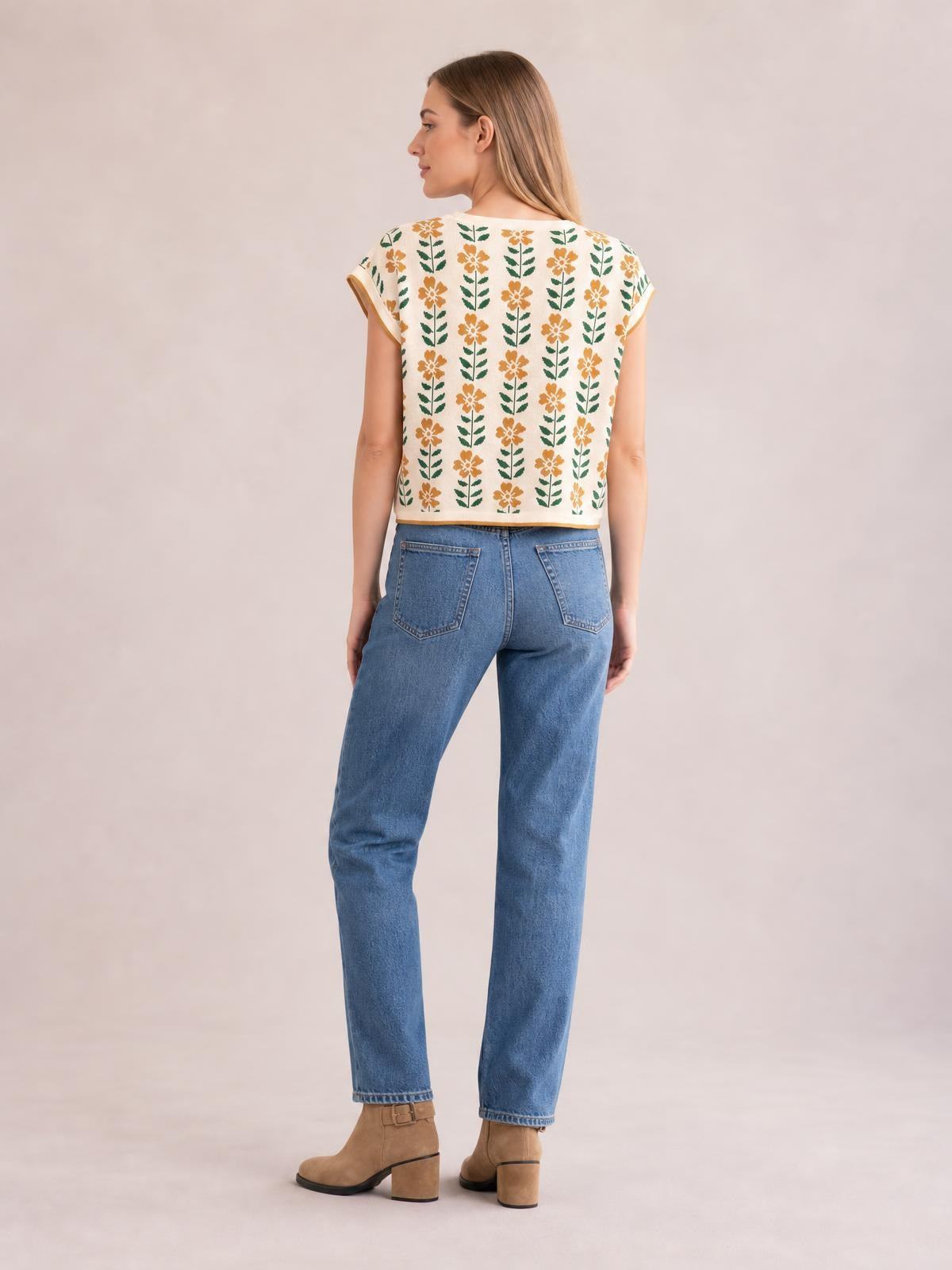 A model faces away in a cream flower-print knit top with a round neck, short sleeves, contrast edging, and a relaxed cropped silhouette.