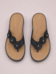Black PU leather flower toe post sandals with layered floral embellishments, tan cushioned footbeds, stitched construction, and low rubber heels.