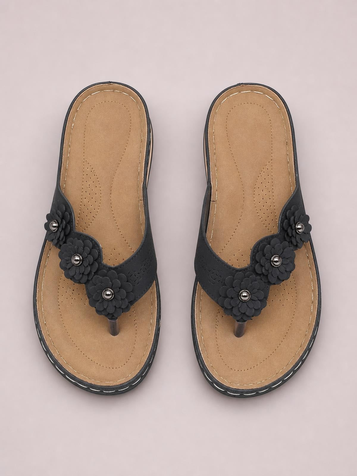 Black PU leather flower toe post sandals with layered floral embellishments, tan cushioned footbeds, stitched construction, and low rubber heels.