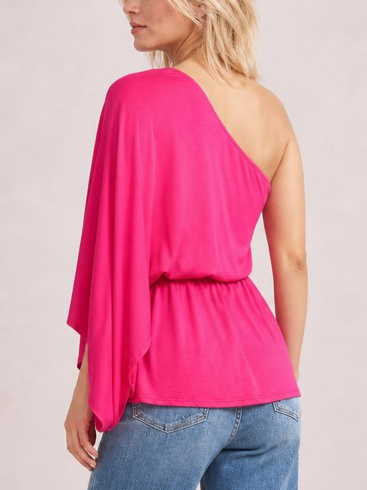 Model shown from the back wearing a bright pink Forever And Always one-shoulder top with an asymmetrical neckline, flowing long sleeve, and relaxed silhouette.