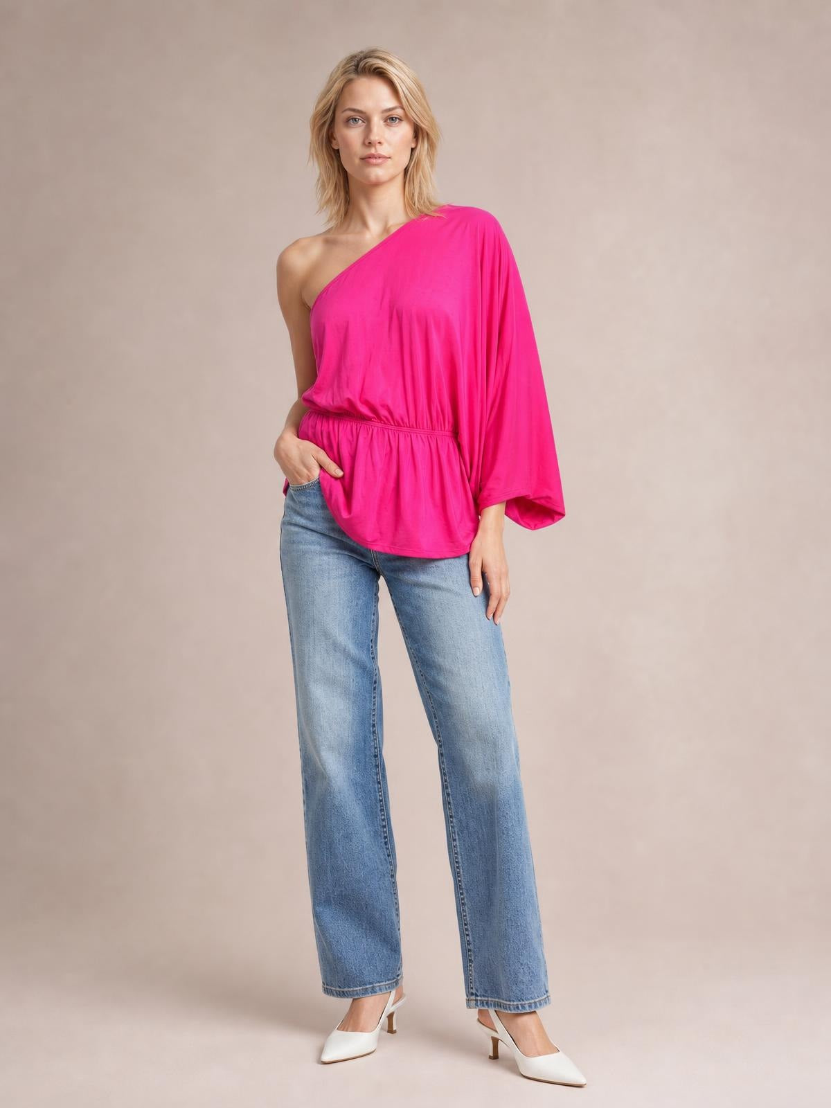 A model poses in a bright pink Forever And Always one shoulder top with an asymmetrical neckline, single long sleeve, gathered waist, and relaxed silhouette.