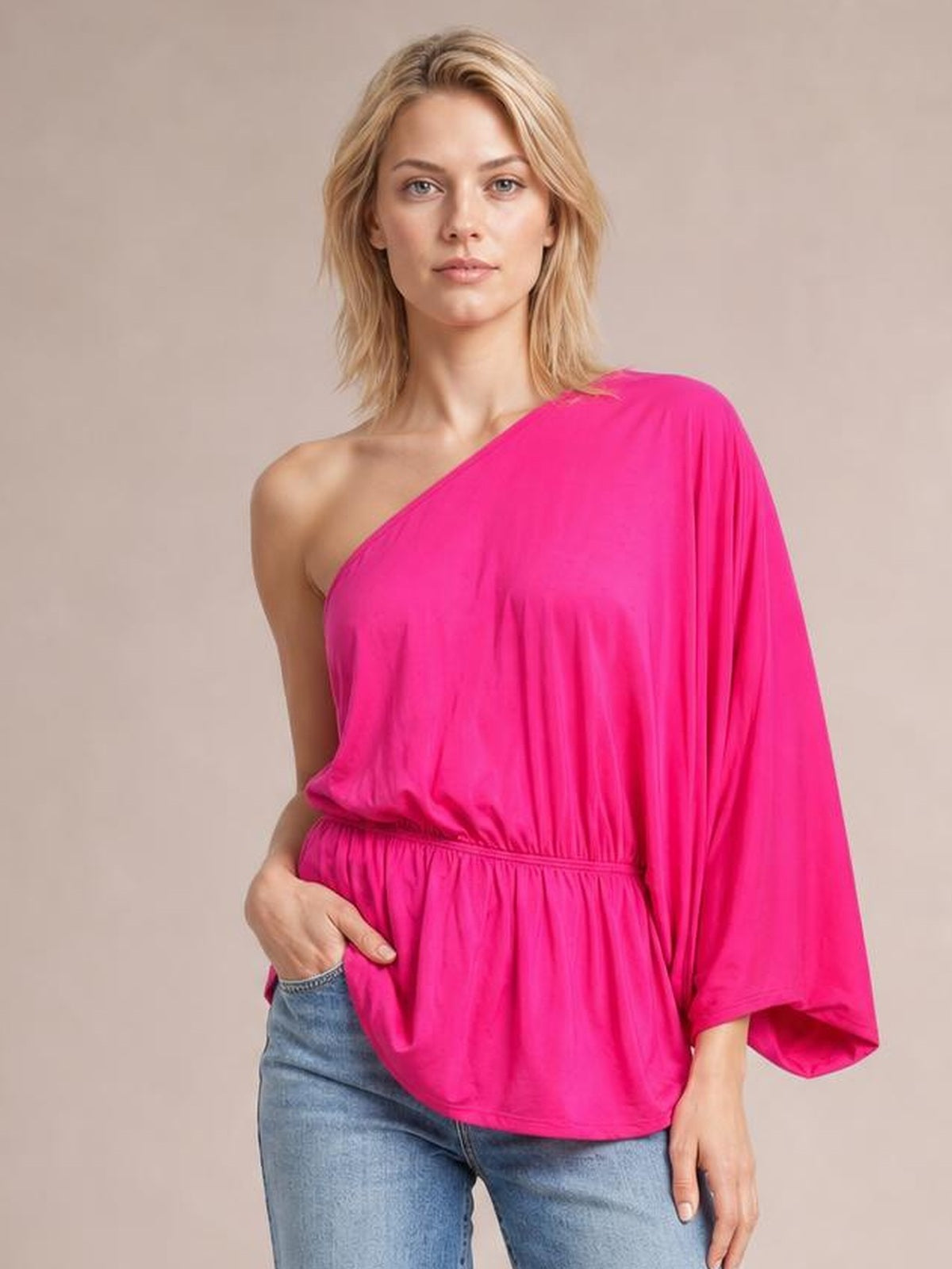 Model poses in a bright pink Forever And Always one-shoulder top with an asymmetrical neckline, single loose sleeve, elastic waist, and relaxed silhouette.