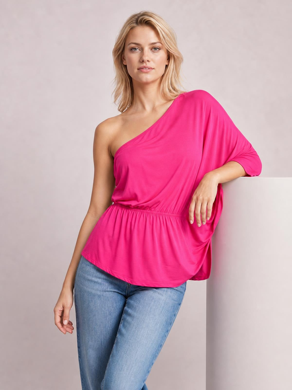 Model poses in a bright pink Forever And Always one-shoulder top with an asymmetrical neckline, single long sleeve, elastic waist, and relaxed regular-length silhouette.
