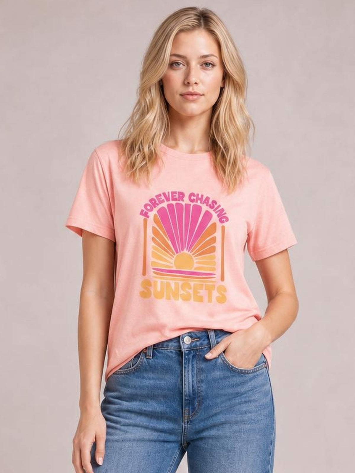Model wearing a pink FOREVER CHASING SUNSETS round neck T-shirt with short sleeves and a relaxed fit, featuring a colorful sunset graphic.