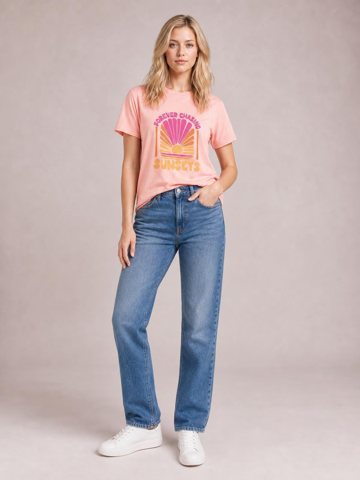 Model poses in a pink round-neck FOREVER CHASING SUNSETS T-shirt with short sleeves, colorful sunset graphic, and a relaxed straight silhouette.
