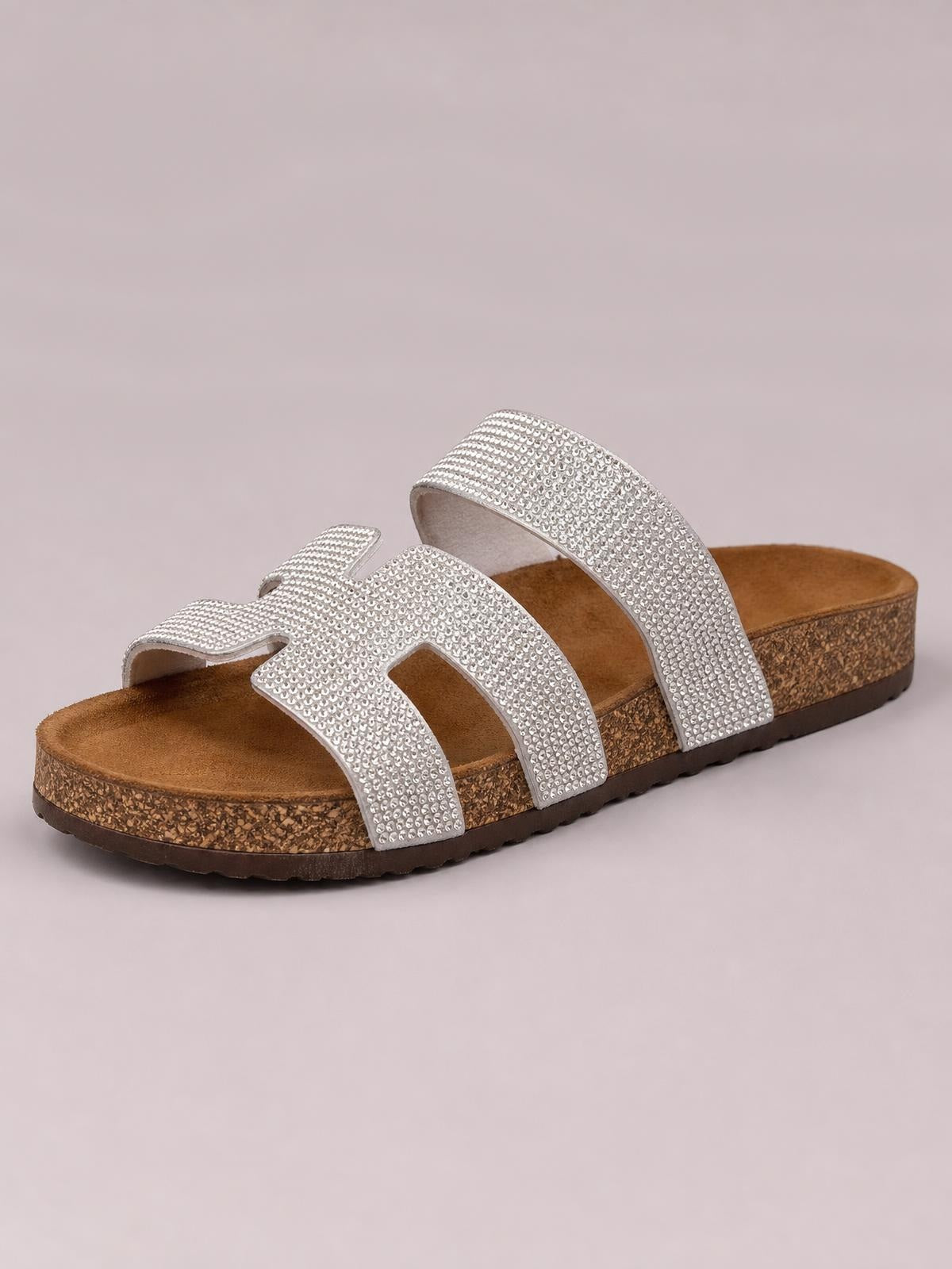 Silver rhinestone open-toe flat sandals feature sparkling multi-strap uppers, cushioned brown footbeds, and sturdy textured soles.