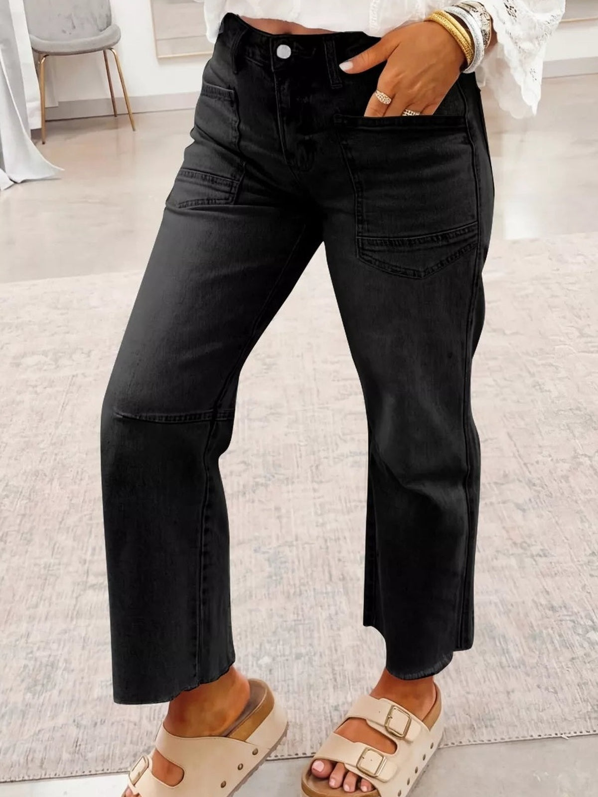 Model wears black cropped straight-leg jeans with multiple pockets and panel stitching, standing with one hand tucked into the front pocket.