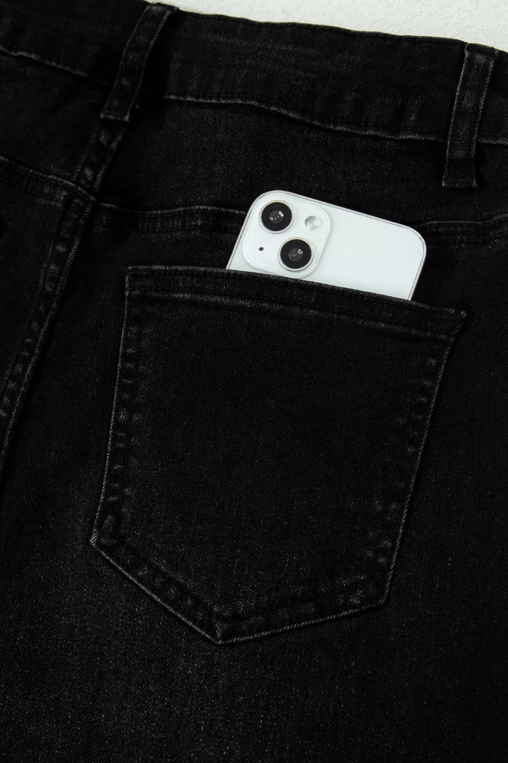 Close-up of black straight-leg jeans showing the waistband, belt loops, tonal stitching, and a structured back pocket with reinforced seams.