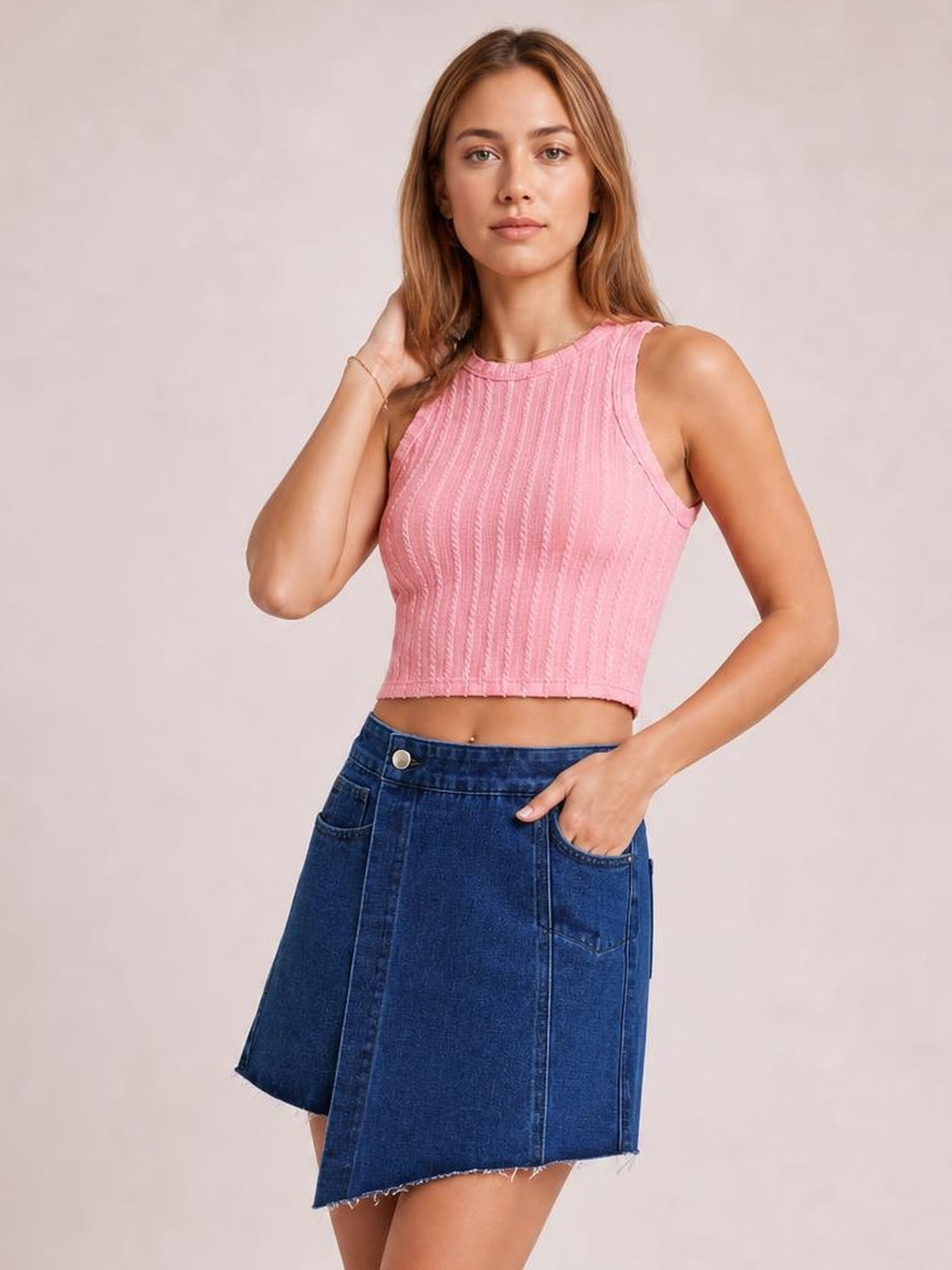 Model poses with one hand in a pocket, wearing a dark blue asymmetrical denim skort with a frayed hem, front pockets, and a structured A-line silhouette.
