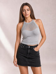 Model wearing a black denim mini skirt with a buttoned front, pockets, straight silhouette, and frayed hem, posing with one hand in a pocket.