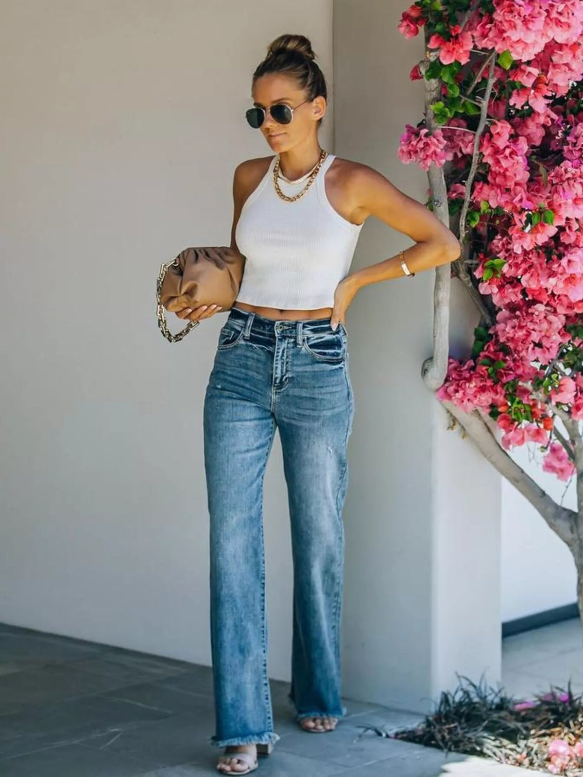 Model poses with one hand in the pocket, wearing blue high-waisted wide-leg jeans with front pockets, a button fly, and frayed raw hems.