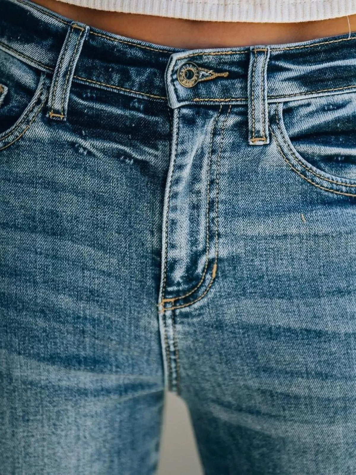 Close-up of blue high-waisted wide-leg jeans showing a button fly, belt loops, contrast stitching, and front pockets with structured construction.