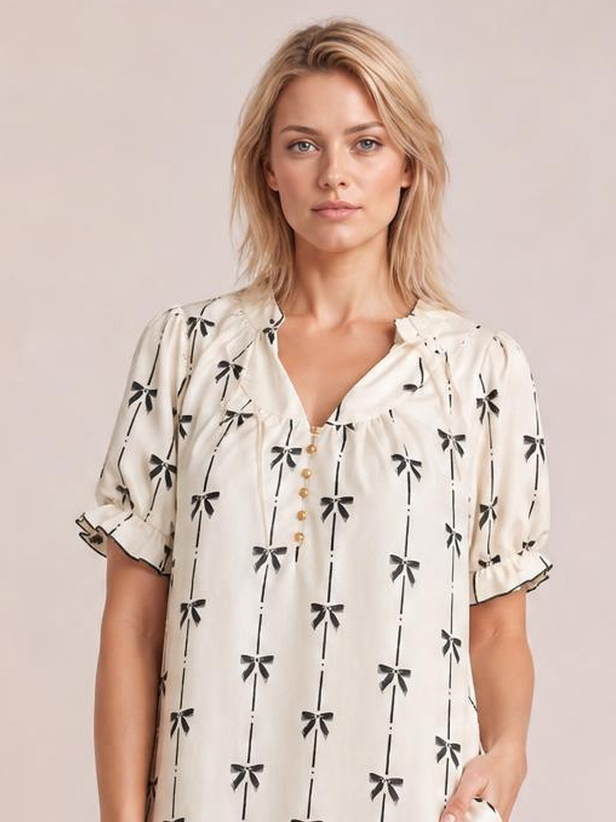 A model wears a cream mini dress with black bow print, a notched frill neckline, short sleeves, front buttons, and a relaxed silhouette.