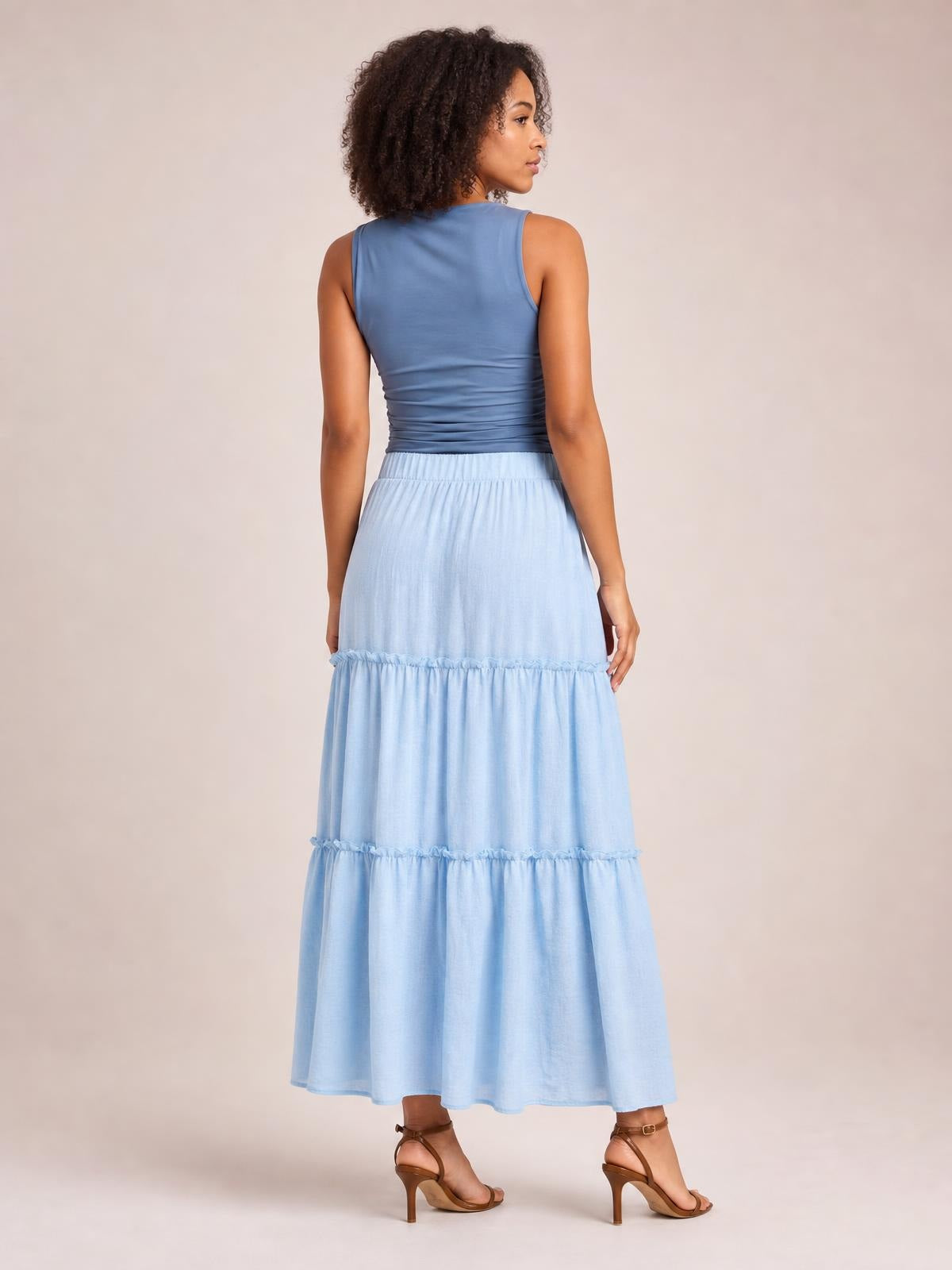 A model poses from behind wearing a light blue Frill Elastic Waist Skirt with a long flowing silhouette, elastic waistband, and tiered frill construction.