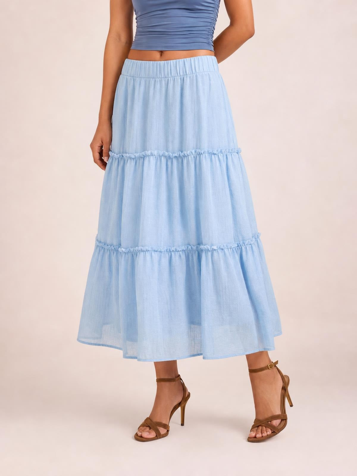 Model poses in a light blue Frill Elastic Waist Skirt with a tiered midi silhouette, gathered elastic waistband, and ruffled seam details.
