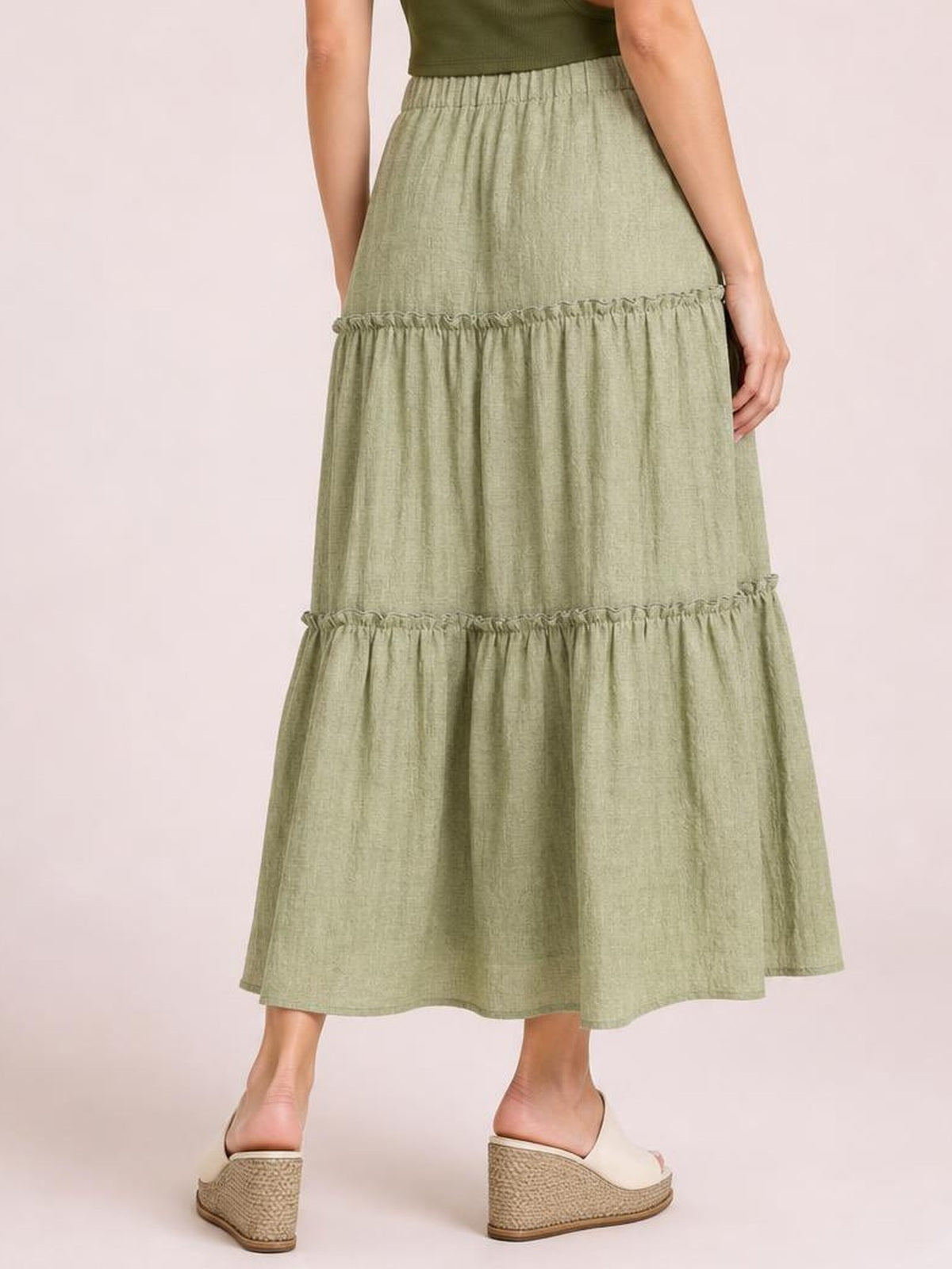 Model shown from behind wearing a sage green Frill Elastic Waist Skirt with a gathered waistband, tiered frill details, lined opaque fabric, and flowing midi silhouette.