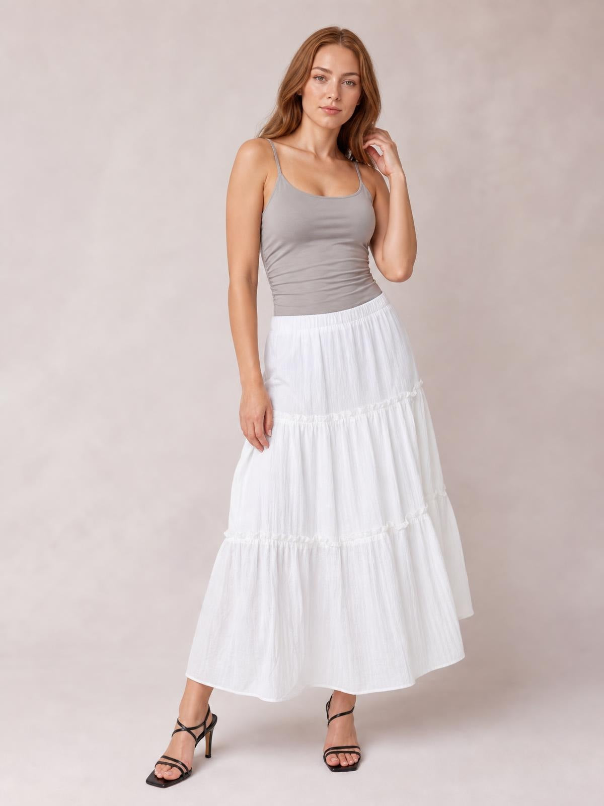 Model poses in a white Frill Elastic Waist Skirt with a tiered, flowing maxi silhouette, multiple ruffled seams, and a comfortable gathered waistband.