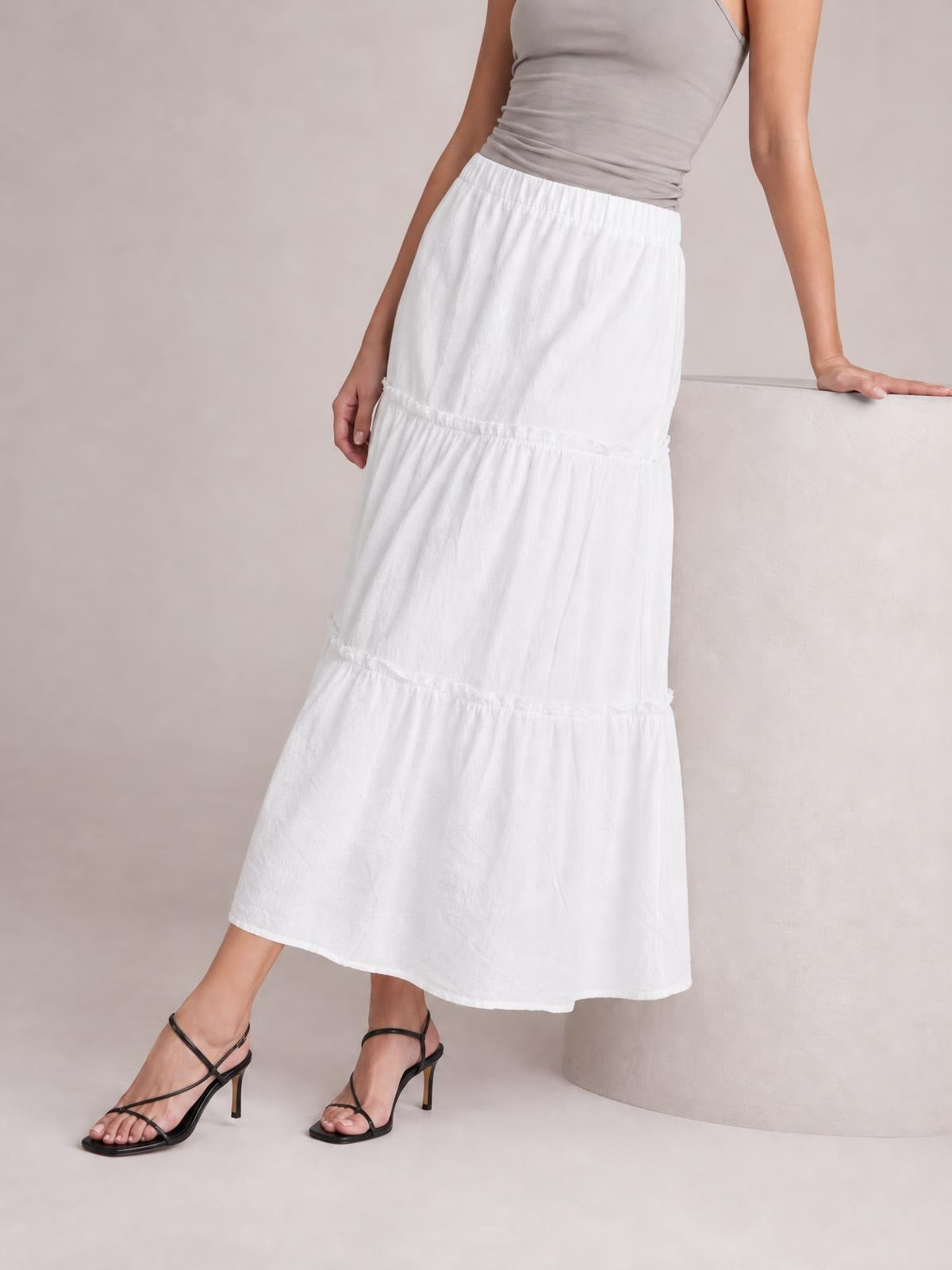 A model poses in a white Frill Elastic Waist Skirt with a gathered waistband, tiered frill construction, lined opaque fabric, and a flowing midi silhouette.