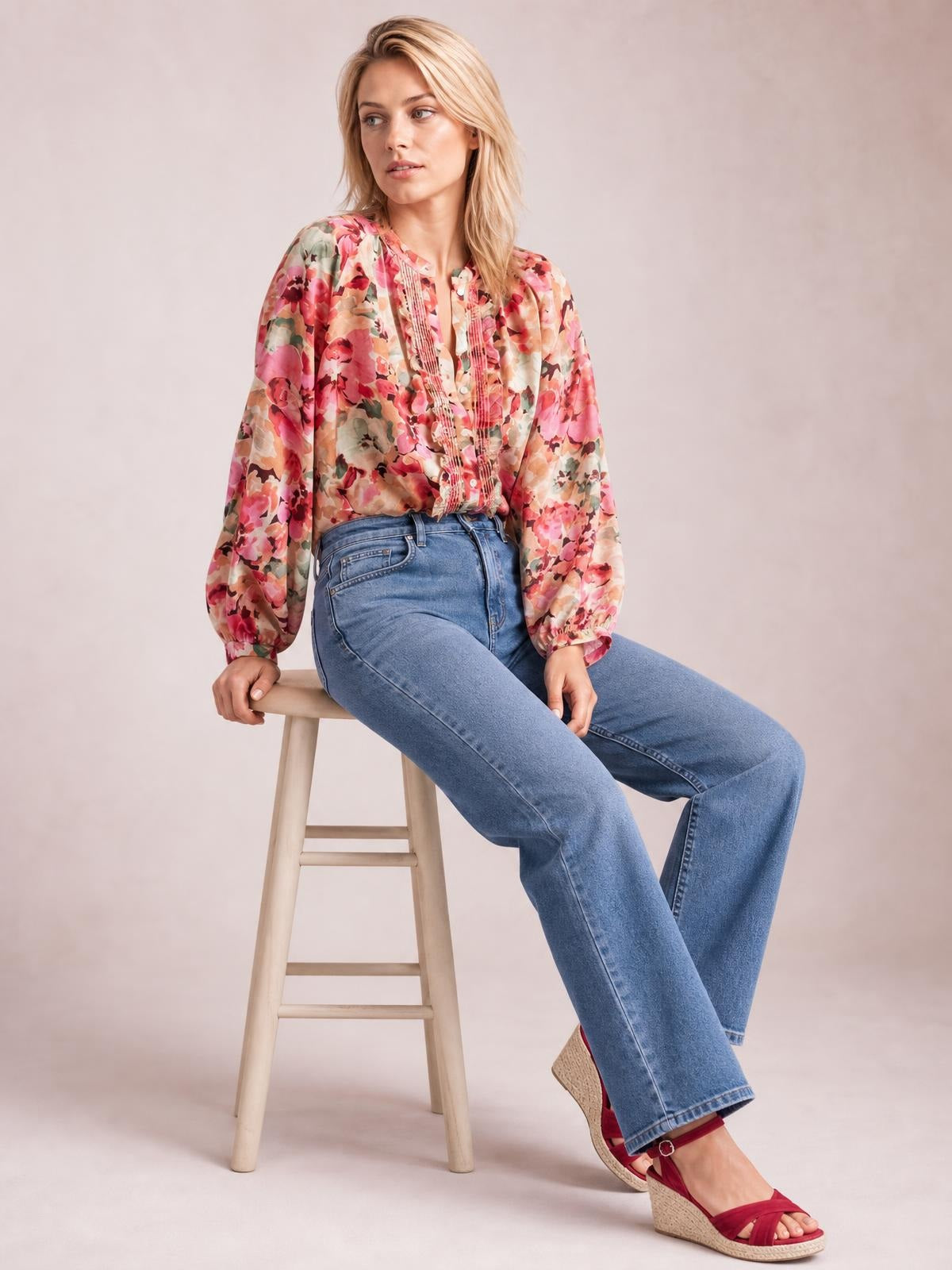 Model sits on a stool wearing an opaque floral button-down shirt with long sleeves, front frill detailing, and a relaxed silhouette.