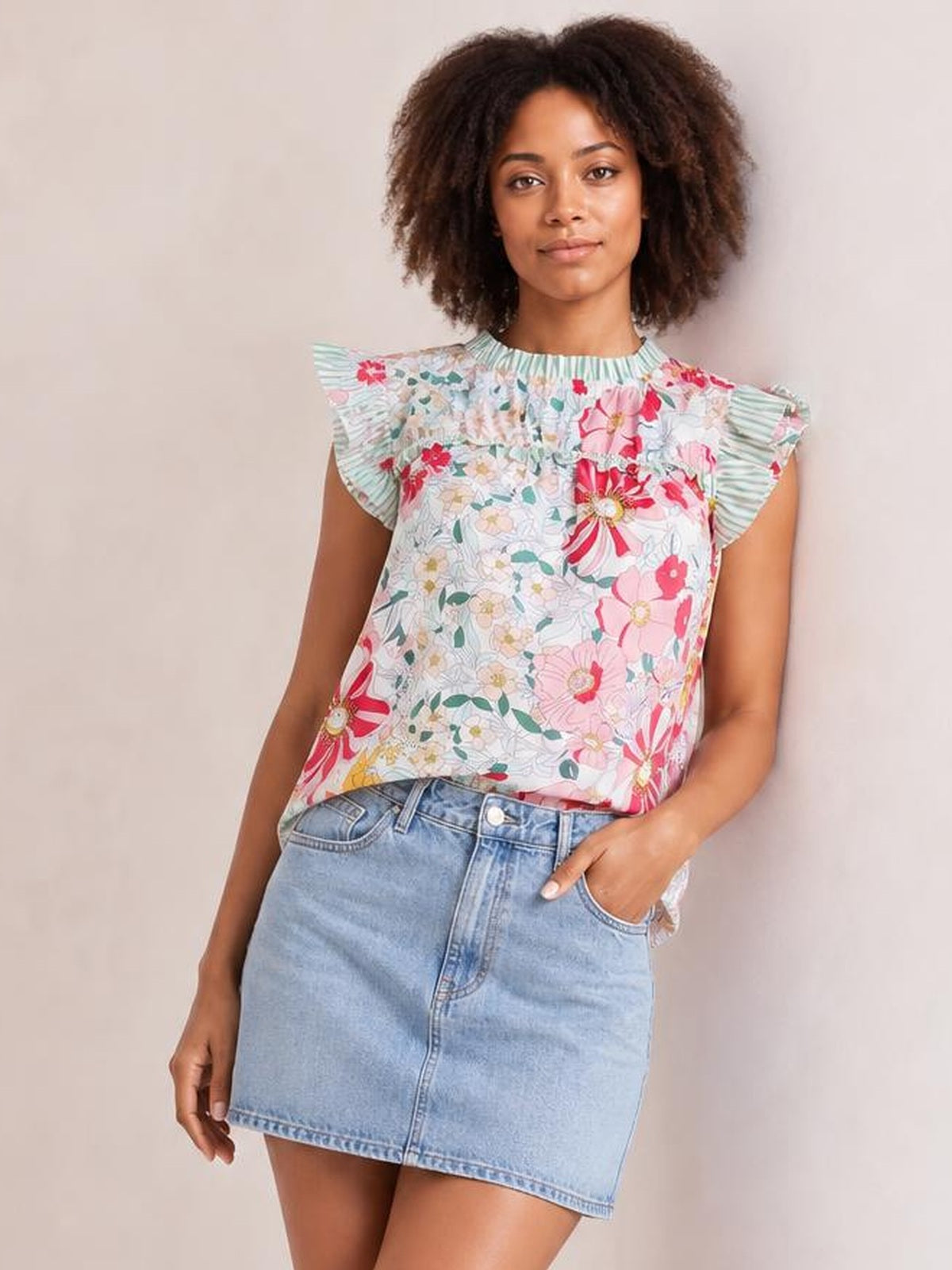 Model wearing an opaque floral print blouse with ruffle cap sleeves, frill detailing, and a relaxed straight silhouette, standing with one hand in her pocket.