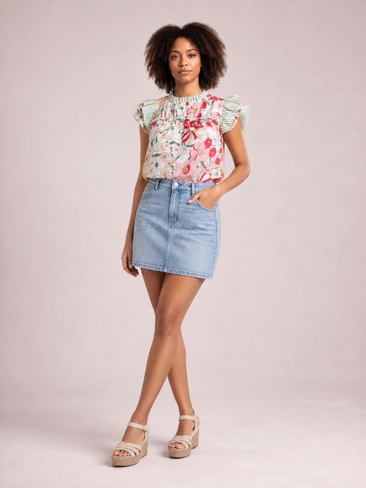 Model wears an opaque floral print blouse with ruffle cap sleeves, frill trim, a gathered neckline, and a relaxed silhouette tucked into a denim skirt.