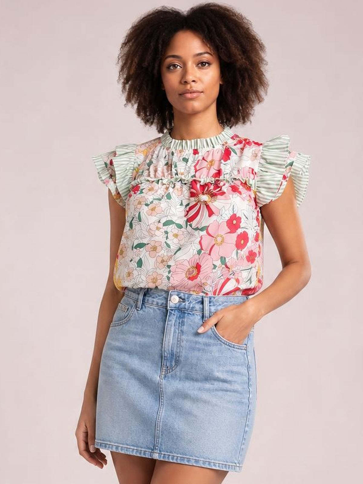 Model wearing an opaque floral print blouse with ruffle cap sleeves, frill neckline, and a relaxed silhouette, paired with a denim skirt.