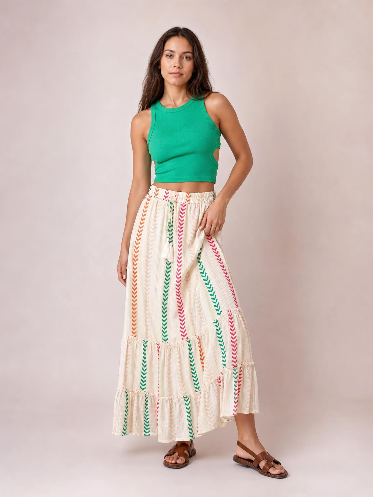Model poses in a flowy cream Frill Printed Maxi Skirt with colorful vertical chevron print, tied waist, and tiered frill construction.