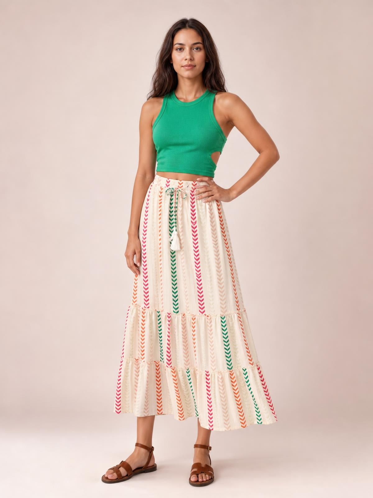 Model poses with one hand on her hip in a flowy printed maxi skirt featuring colorful vertical stripes, a tied waist, and tiered frill details.