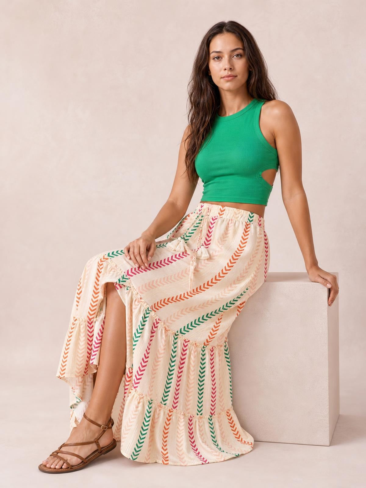 Model seated in a flowy cream printed maxi skirt with colorful chevron stripes, tied waist, and tiered frill construction.