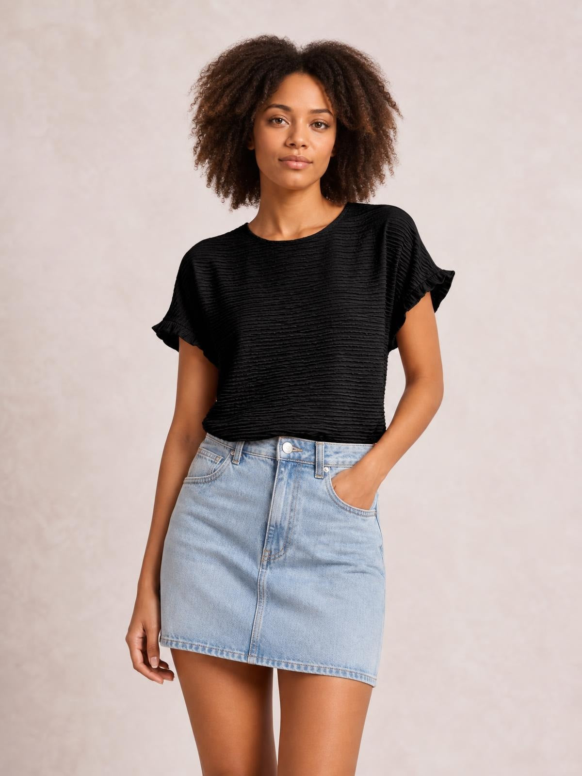 A model stands wearing a black round-neck blouse with short cap sleeves, frill trim, a textured finish, and a relaxed straight silhouette.