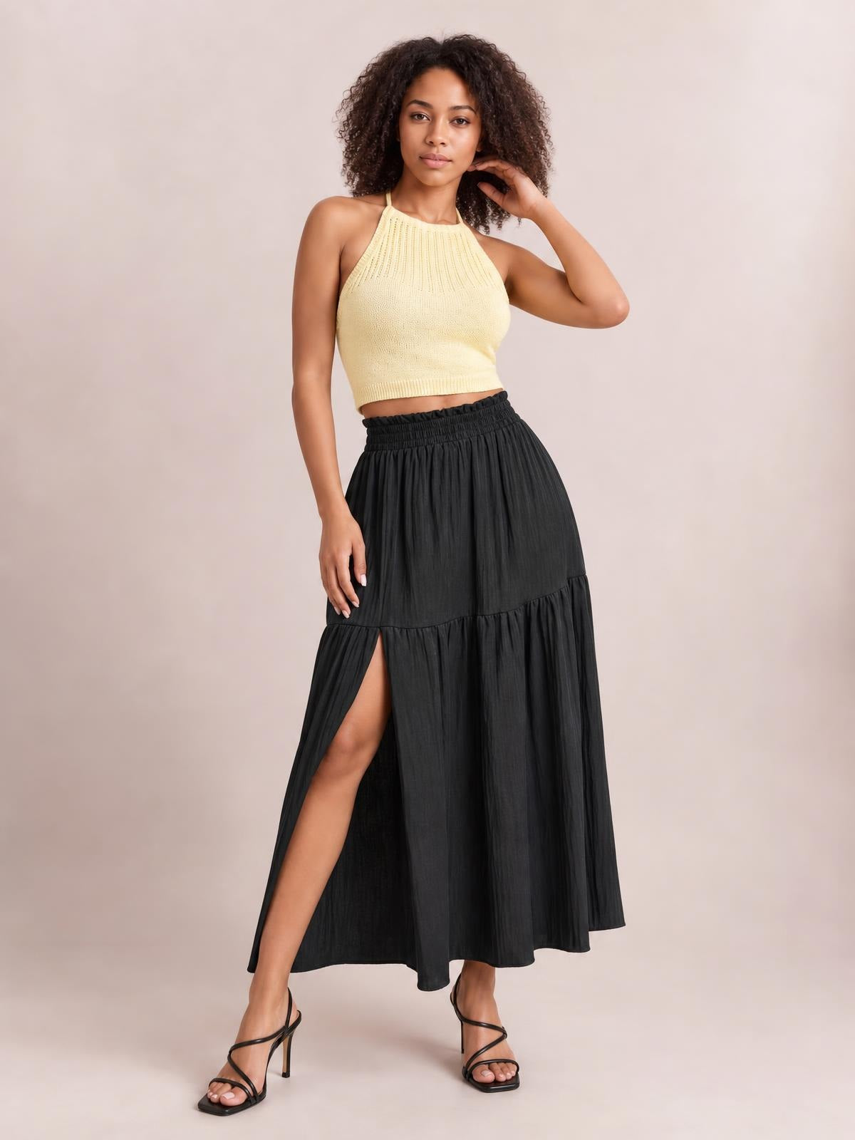 A model poses in a black Frill Slit Skirt with an elastic waistband, flowing maxi silhouette, tiered frill hem, and high side slit.