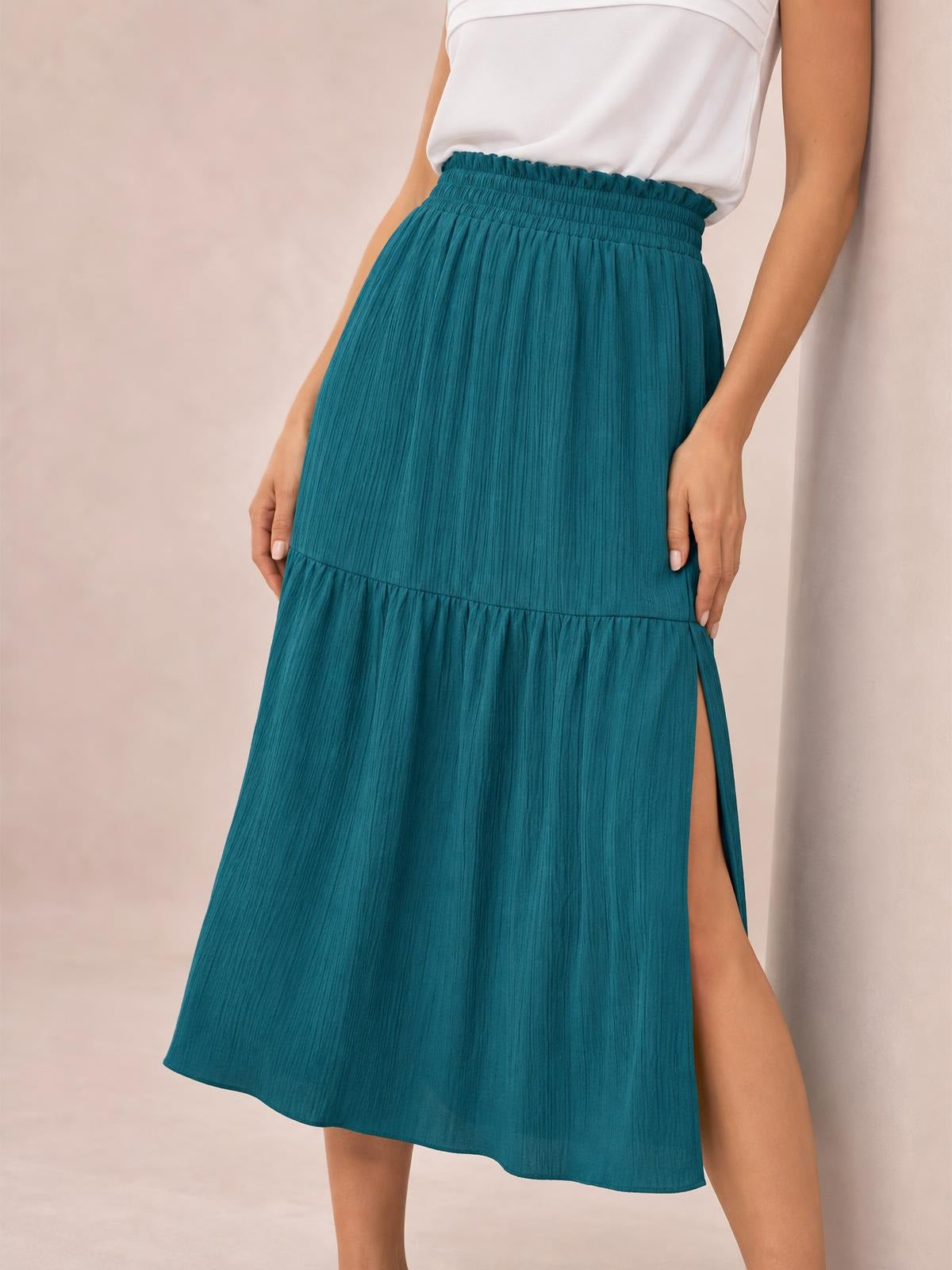Model wears a teal Frill Slit Skirt with a gathered elastic waistband, tiered construction, flowing midi silhouette, and a high side slit.