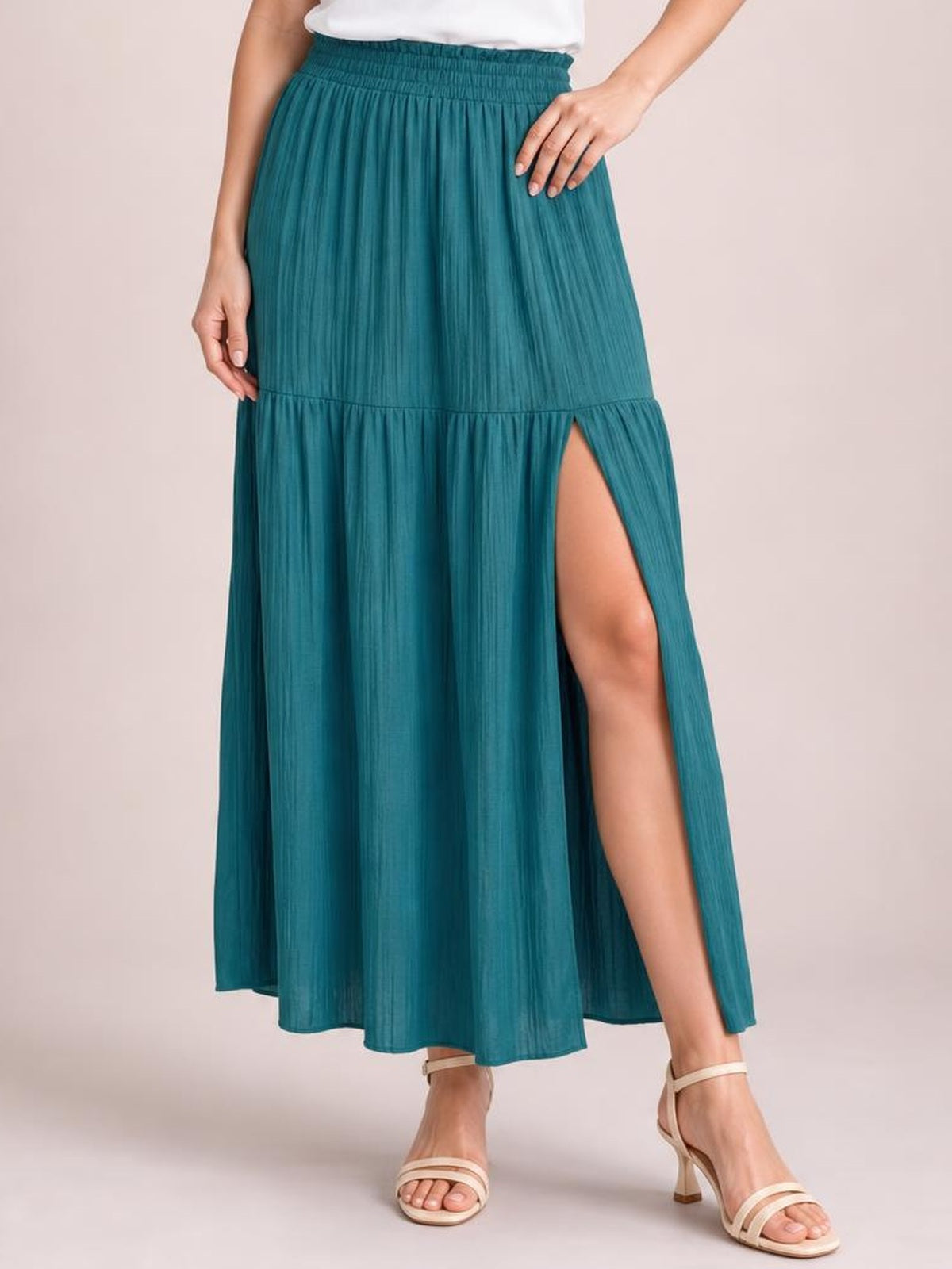 A model poses in a teal Frill Slit Skirt with a smocked waistband, flowing maxi silhouette, gathered frill tier, and high side slit.