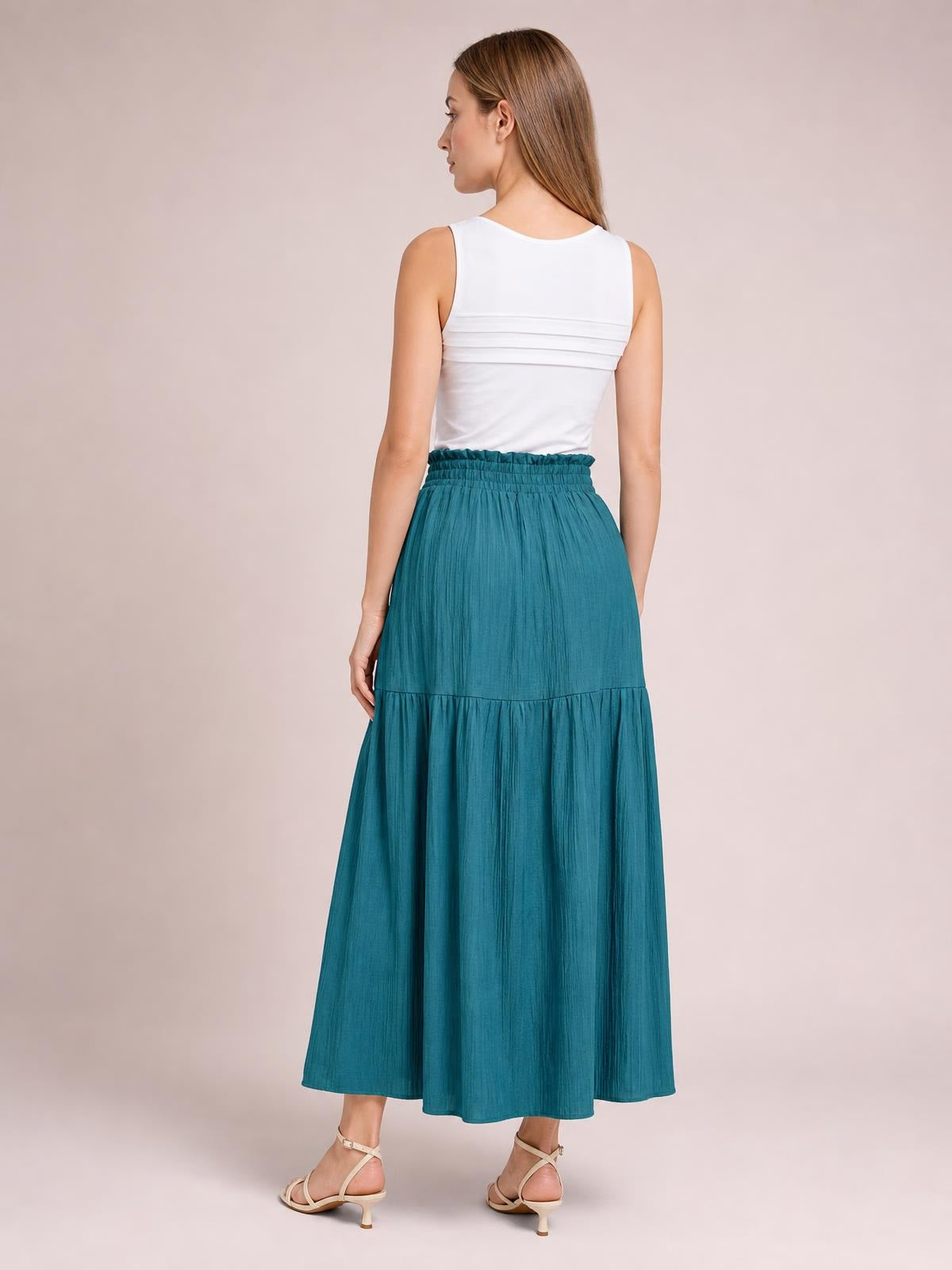 A model shows the back of a teal Frill Slit Skirt with a gathered elastic waistband, flowing maxi silhouette, and tiered frill construction.