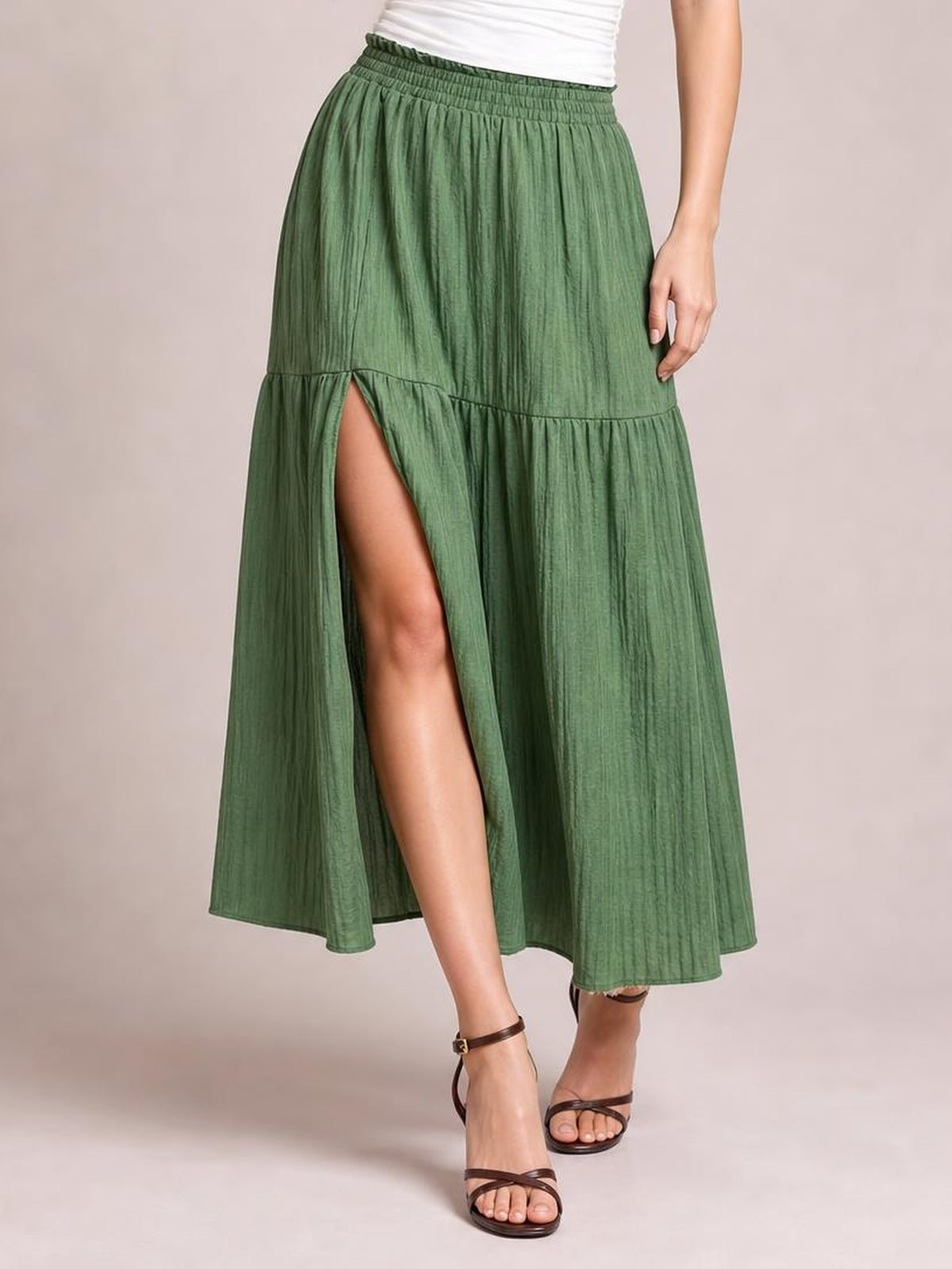 A model wears a green Frill Slit Skirt with an elastic waist, gathered tiered silhouette, flowing midi length, and a high front slit revealing one leg.