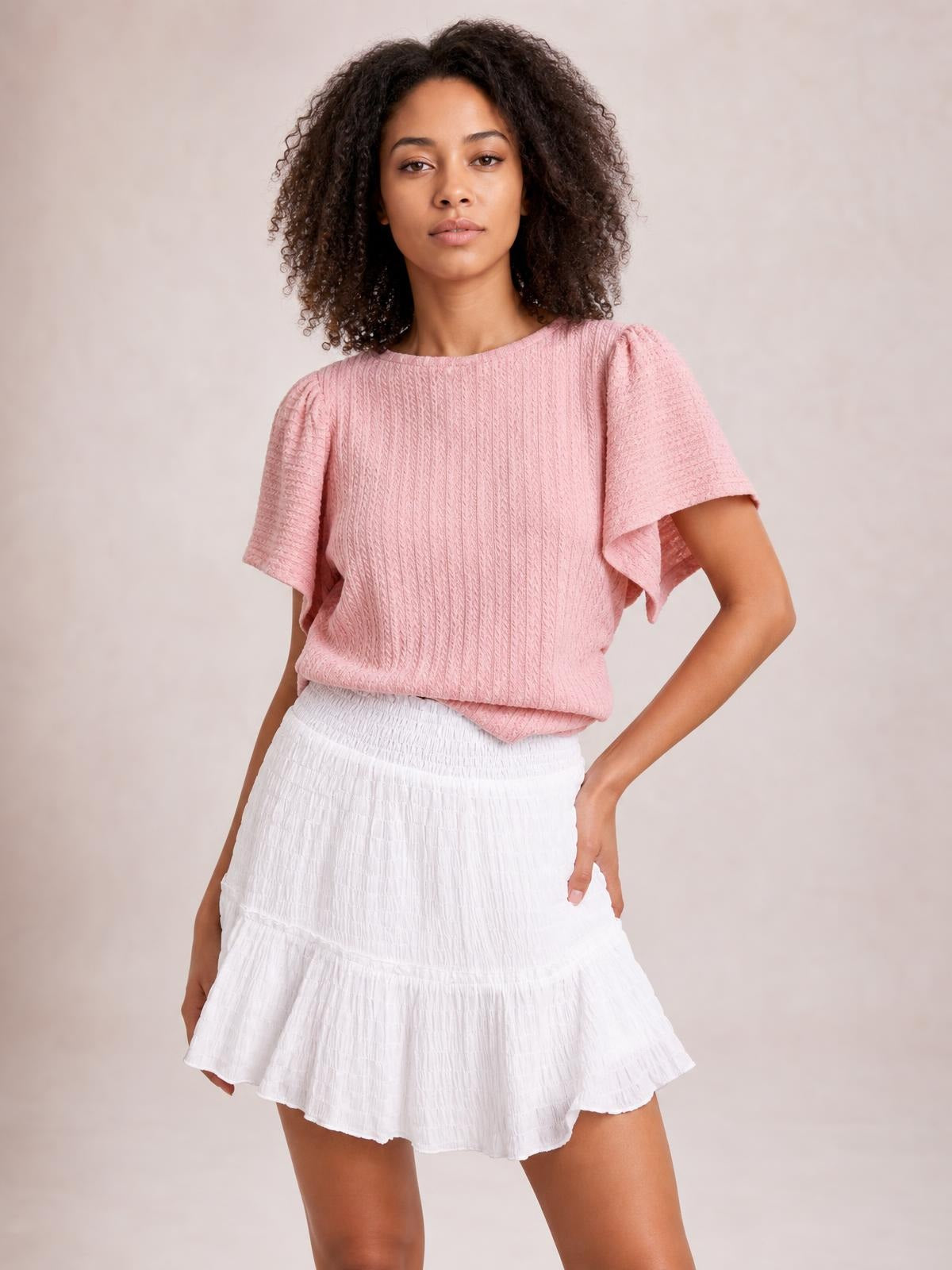 Model wearing a white Frill Tiered Mini Skirt with a smocked waist, textured tiered construction, and flared frilled hem, posing with one hand on her hip.