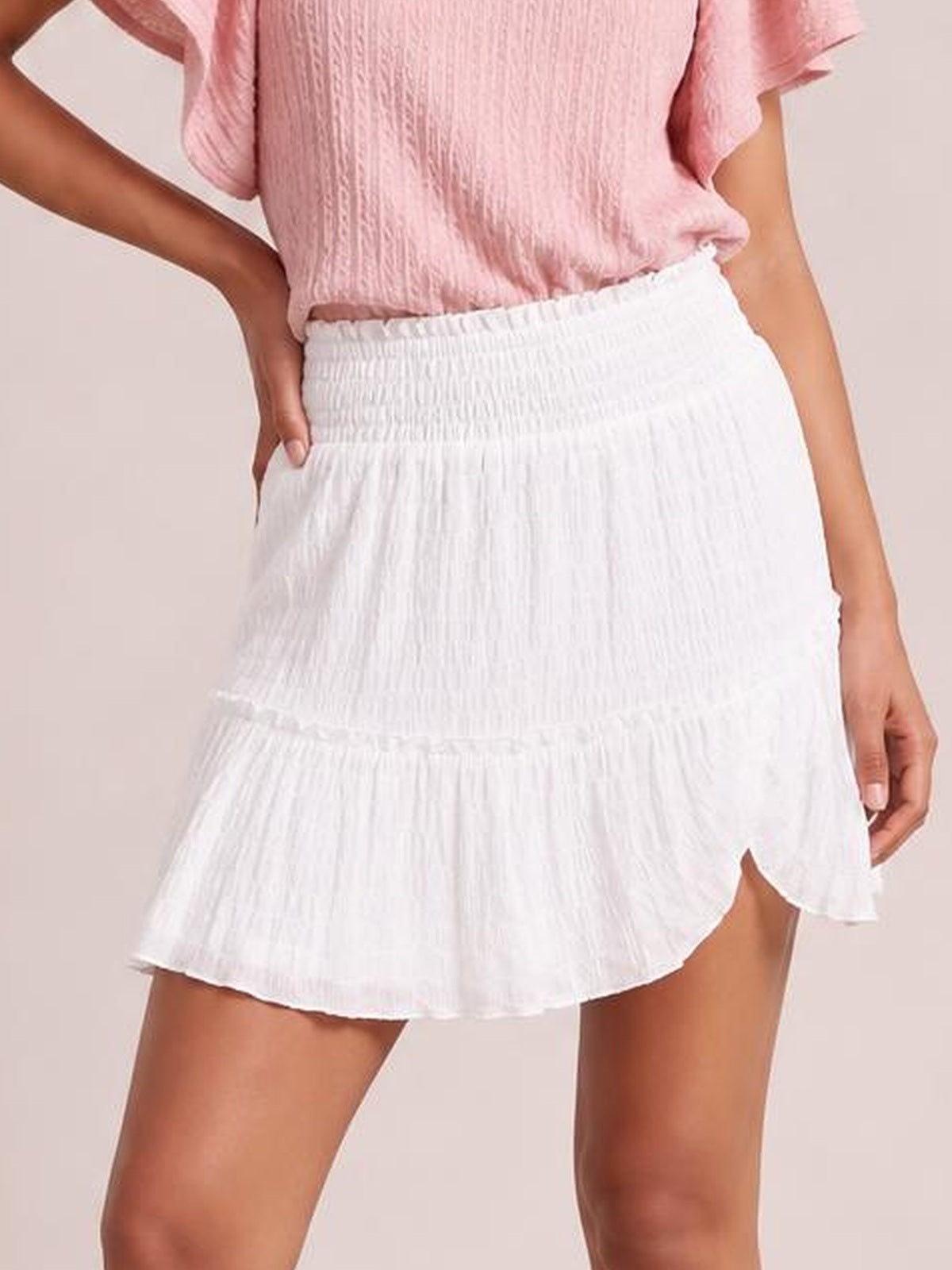 A model poses in a white Frill Tiered Mini Skirt with a smocked waistband, tiered construction, and playful ruffled hem.