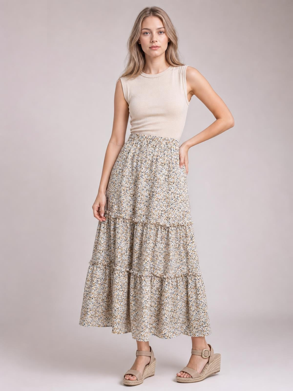 A model poses with one hand on her hip wearing a flowy beige printed skirt with a gathered waist, tiered silhouette, and frill-trimmed panels.