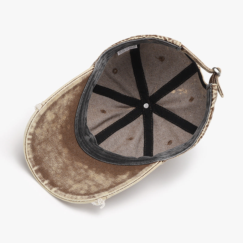 A tan cotton baseball cap with a worn finish, curved brim, frayed fringe detailing along the front edge, six-panel construction, and an adjustable metal-buckle back strap.