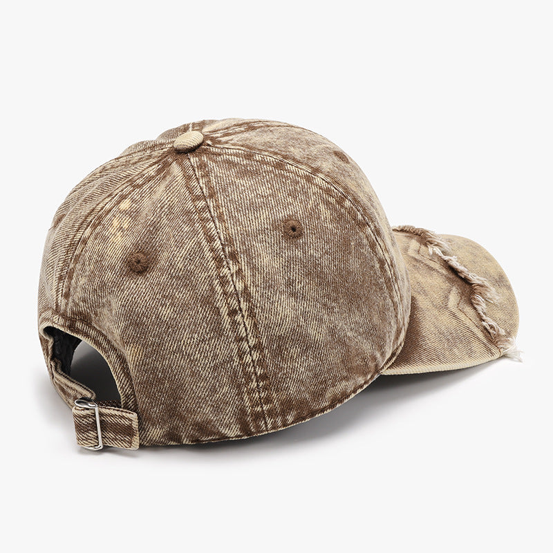 Distressed tan cotton baseball cap shown from the back, featuring a six-panel crown, open back, adjustable metal-buckle strap, curved brim, and fringe along the front edge.