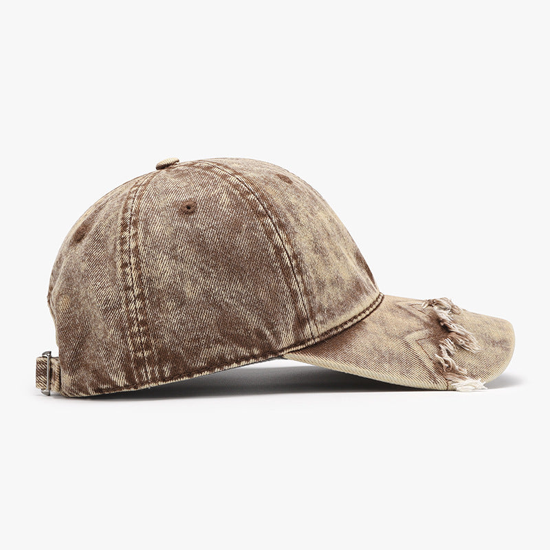 Distressed tan cotton baseball cap with a classic six-panel silhouette, curved brim, fringe trim along the front edge, and an adjustable metal buckle strap.