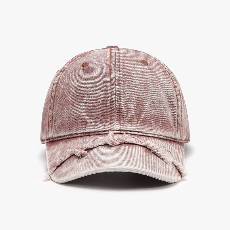 A dusty pink cotton baseball cap features a classic six-panel silhouette, curved brim, topstitching, and distressed fringe detailing along the front edge.