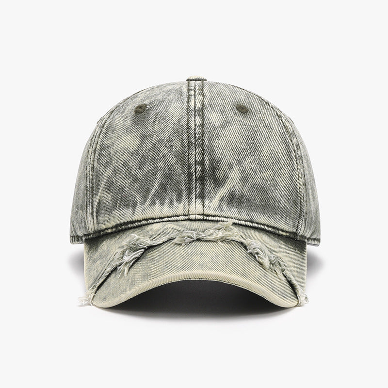A washed gray cotton baseball cap features a classic six-panel crown, curved brim, visible seam construction, and distinctive fringe detailing along the front edge.