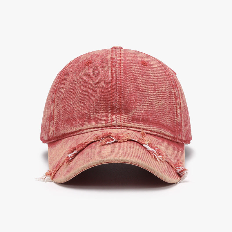 A faded red cotton baseball cap features a classic six-panel construction, curved brim, adjustable fit, and distressed fringe detailing along the front edge.