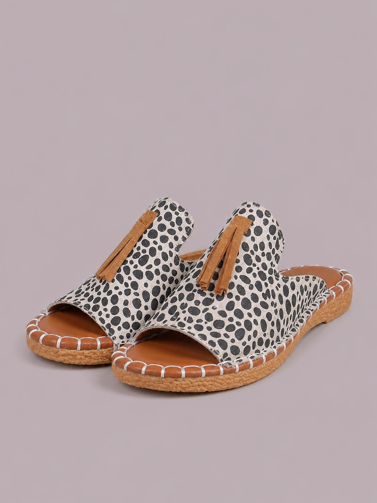 Leopard-print open-toe flat sandals feature tan fringe straps, cushioned footbeds, white contrast stitching, and textured woven soles.
