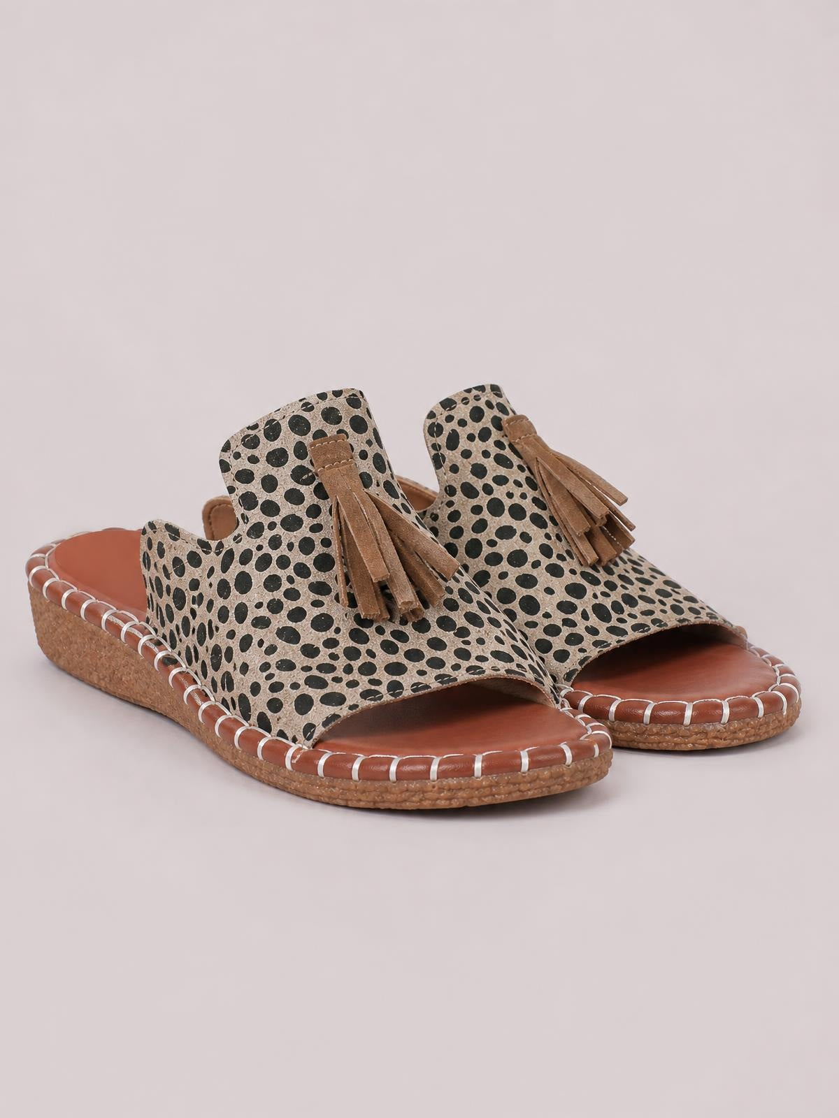 Leopard-print open-toe flat sandals feature tan fringe tassels, wide upper straps, cushioned footbeds, and textured woven soles with stitched trim.
