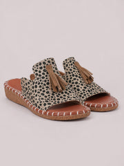 Leopard-print open-toe flat sandals feature tan fringe tassels, wide upper straps, cushioned footbeds, and textured woven soles with stitched trim.
